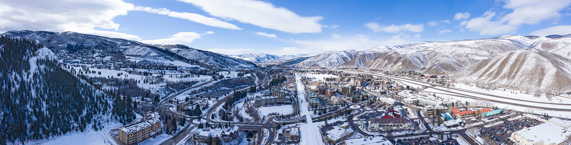 Drone shot of Vail Valley, Colorado in the winter, with snow covering trees, mountains, buildings and roads off in the distance